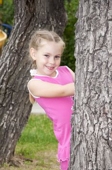 portrait young girl peeping out tree, in summer park