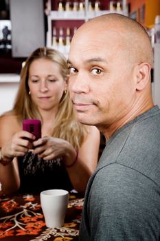 Bored man with woman on cell phone in coffee house