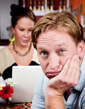 Bored man with woman on laptop computer in coffee house