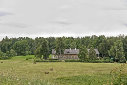 Old farm house and a field with haystacks in cloudy summer day