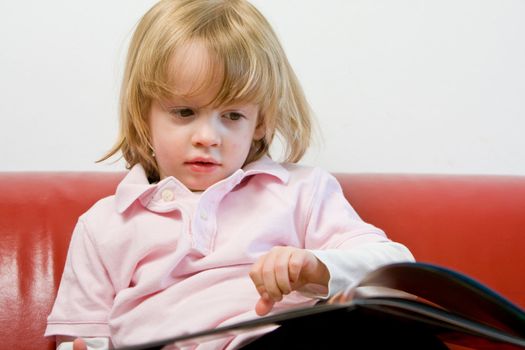 Cute young caucasian boy with blond hair studying or reading a book