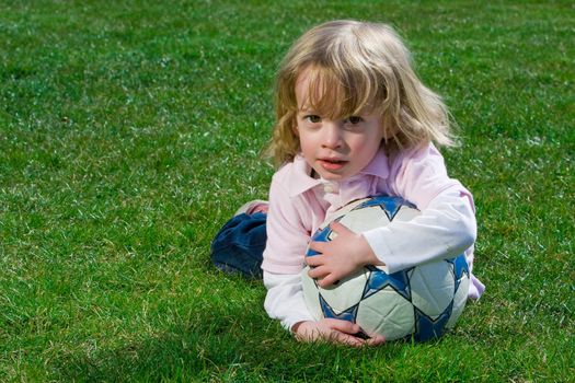 Cute young caucasian boy playing football or soccer outdoors