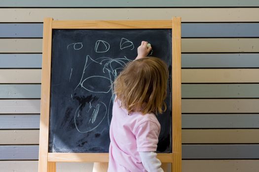 Cute young caucasian boy writing on a blackboard in school or kindergarten