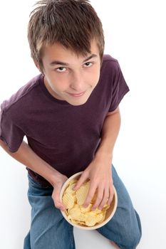 A boy sitting down and eating crinkle cut potato crisps.  