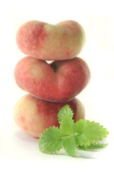 three fresh mountain peaches with lemon balm on white background