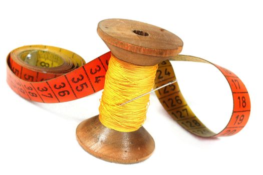 old spool of thread with needle and measuring tape on white background
