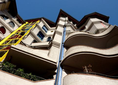 Eccentric facade of a building with strange and colored balconies and windows viewed from down with deep blue sky