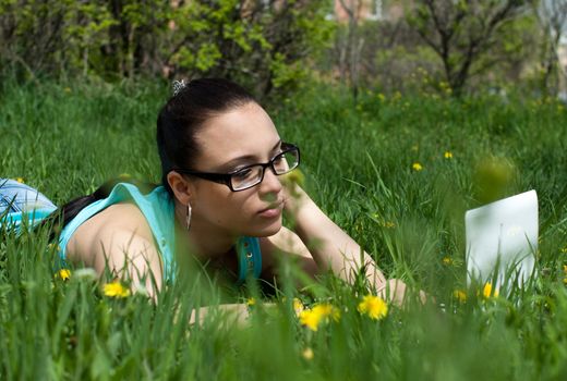 Photo of a girl with a laptop, on a background of flowers and green grass