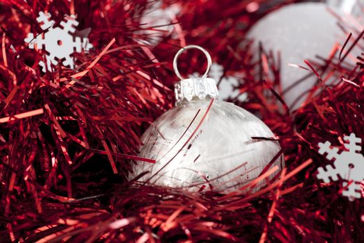 Silver christmas ball ornament sitting in red garland with silver snowflake shapes.