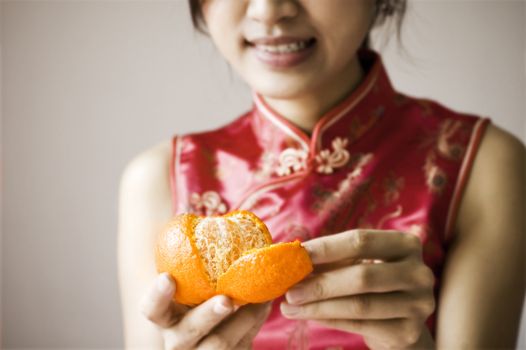 Oriental girl with cheongsam costume peeling a tangerine