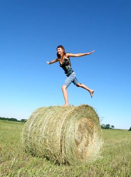 young girl costs on one foot on a hank of yellow hay