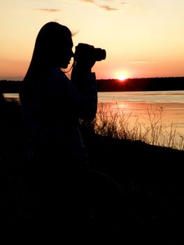 The girl the photographer against a sunset does a nature picture     