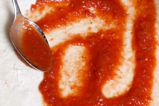 A hand smearing out pizza sauce