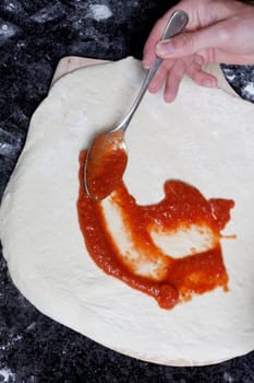 A hand smearing out pizza sauce