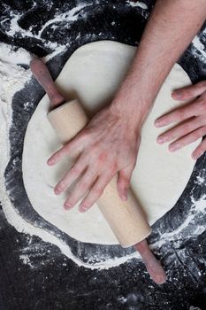 A rolling pin flattening a pizza