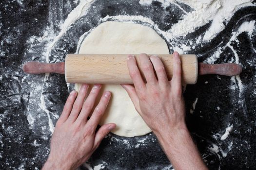 A rolling pin flattening a pizza