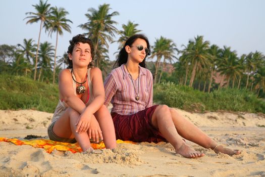 Two pretty girls sitting on the beach sand over sunset in Goa