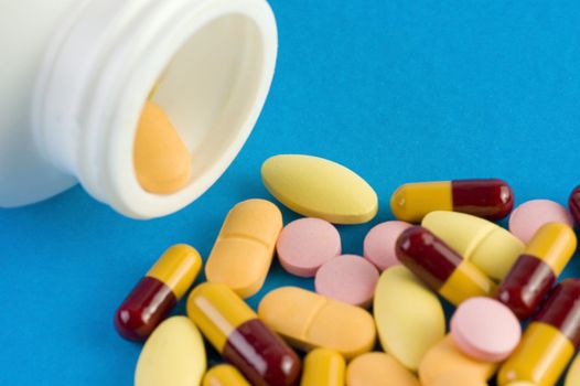Pills spilled out of a bottle and scattered on blue background.