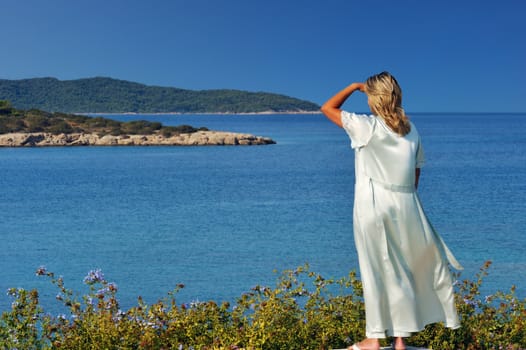 A blond beautiful woman is gazing at the spectacular view of the Greek islands during a clear morning of her summer holidays