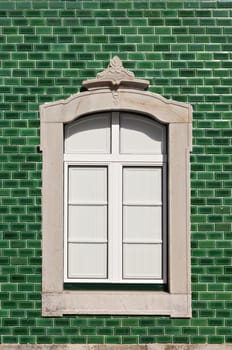 Traditional stone decorated window in a green tile background, Algarve, Portugal