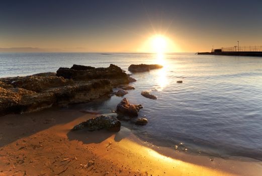 A very bright sunrise over a Mediterranean rocky seascape.  