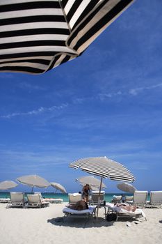 Big umbrellas are staked into the sand for beach goers in sunny Miami, Florida.