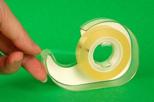 Image shows female fingers pulling a piece of sticky tape from a plastic dispenser