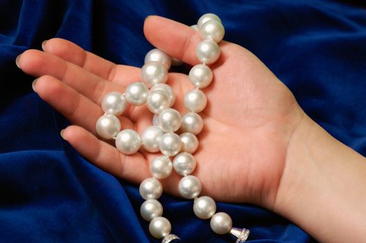 Image shows a female hand demonstrating a pearls necklace, against a blue velvet background