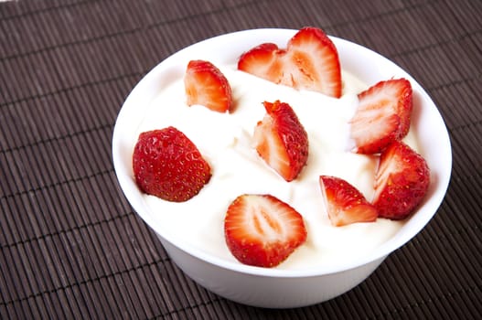 cut slices of a strawberry in a cup with a cream, bamboo mat a back background