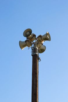 Four sirens on a pole with blue sky in the background.