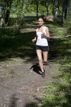 young woman jogging in the park in summer, trees and grass background