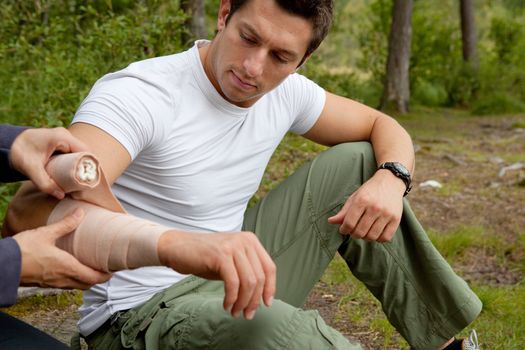 A woman applying an arm bandage on a male camper - focus on male face