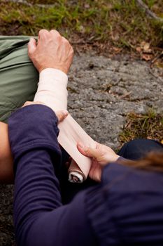 A woman applying an arm bandage on a male camper - focus on male face