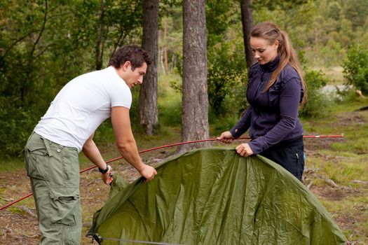 A man and woman setting up a tent in the forest