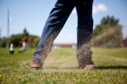 A golf swing on a driving range with sand in the air