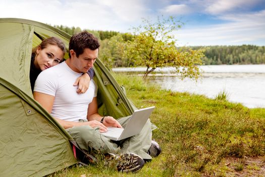 A couple looking at a computer while camping in a tent