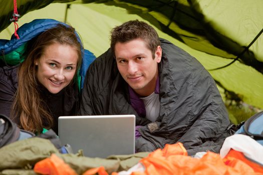 A happy couple in a tent using a computer looking at the camera