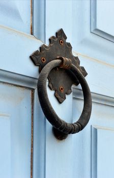 An old weathered door knocker from a light blue painted wooden door