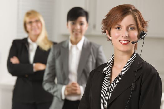 Pretty Red Haired Businesswoman with Headset and Colleagues Behind in Office Setting.