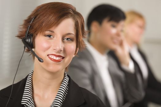 Pretty Red Haired Businesswoman with Headset and Colleagues Behind in Office Setting.