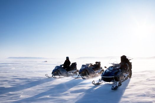 A winter landscape with blowing snow and three snowmobiles.