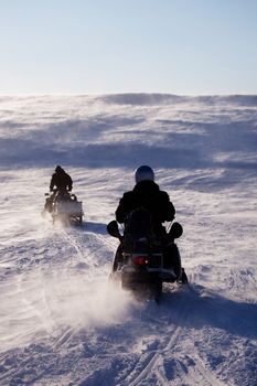 Two people riding up a hill on snowmobiles