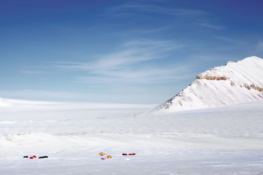 A winter wilderness expedition on a mountain landscape, tents in the distance