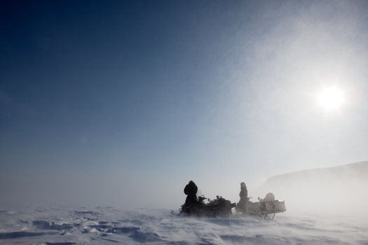 A pair of snowmobiles in a winter blizzard with blowing snow