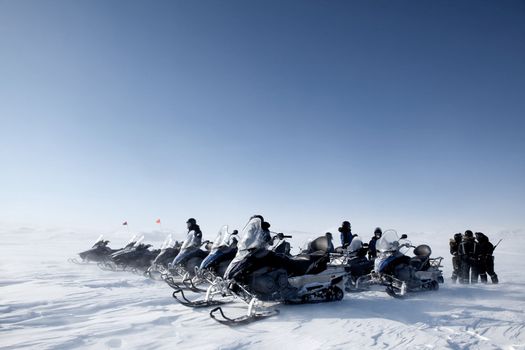 A group of snowmobiles travelling accross a barren winter landscape