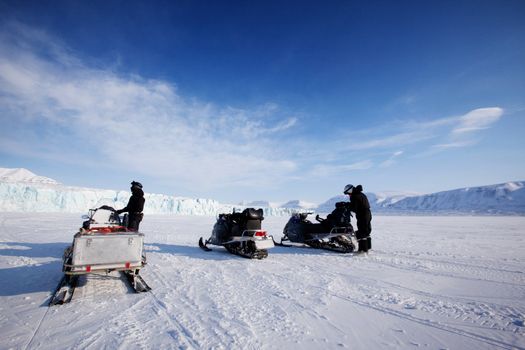 Three snowmobiles in front of a glacier, Svalbard, Norway