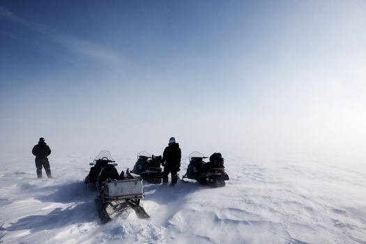 A blowing snow landscape with three snowmobiles on an expedition