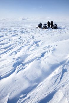 A barren winter landscape with a group of people on a snowmobile expedition