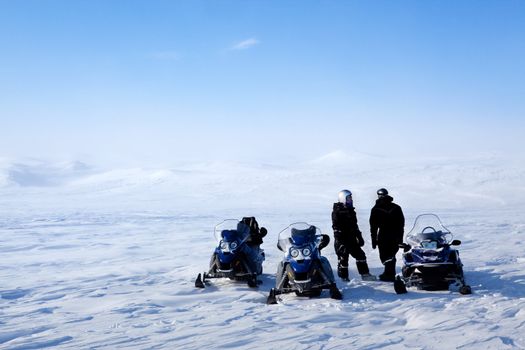 A barren winter landscape with a group of people on a snowmobile expedition