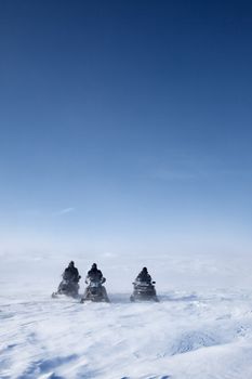 Three snowmobiles on a winter landscape with blowing snow